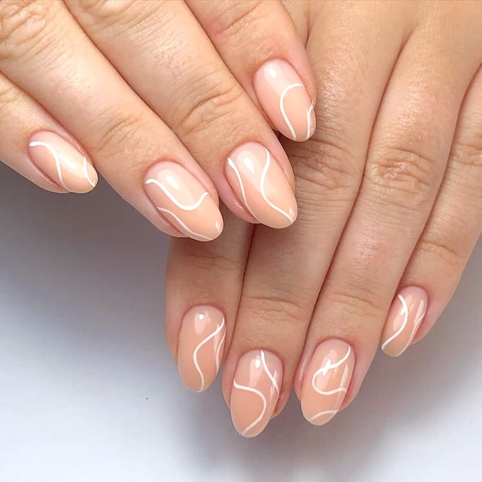 Thin white swirl nude almond nails.