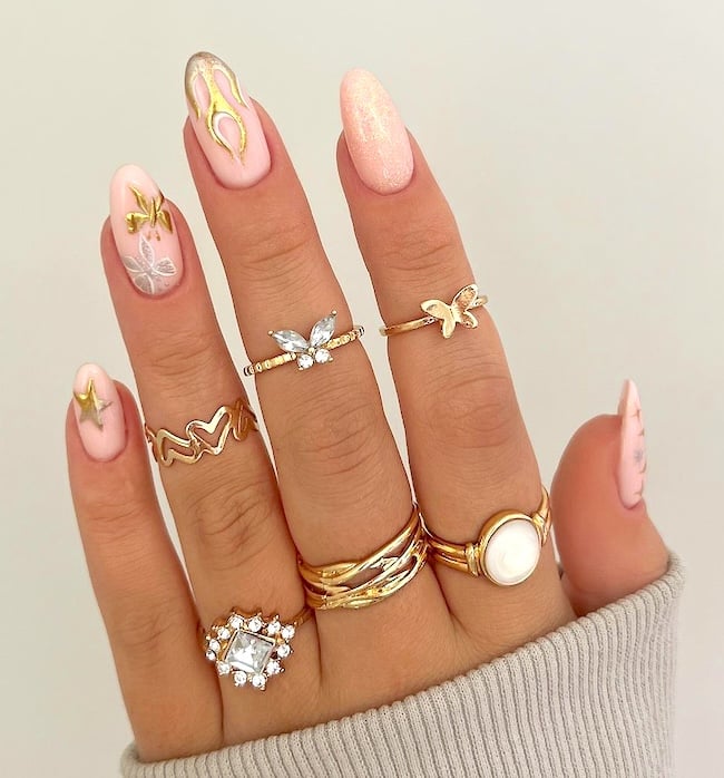 Gold and pink nail art on pretty almond nails with gold rings.