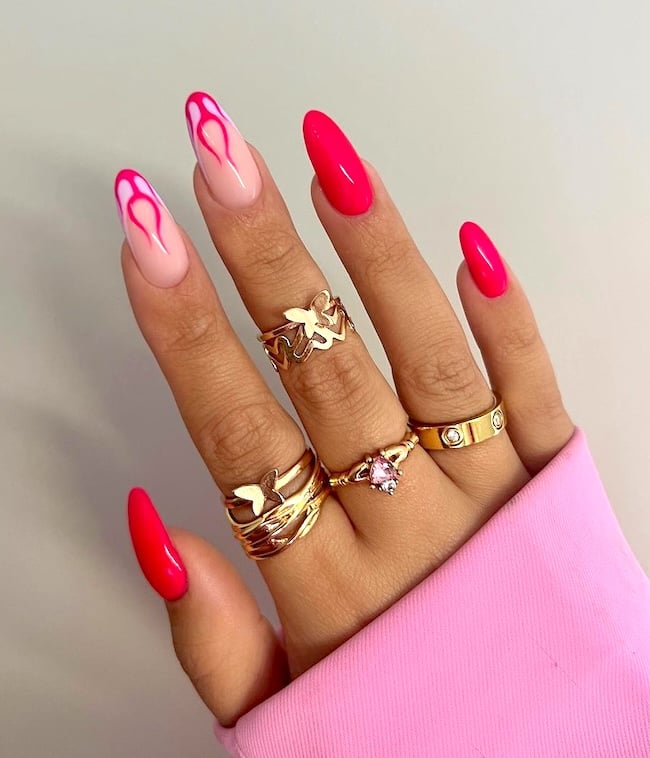 Hot pink flame almond nail on hand wearing gold rings.