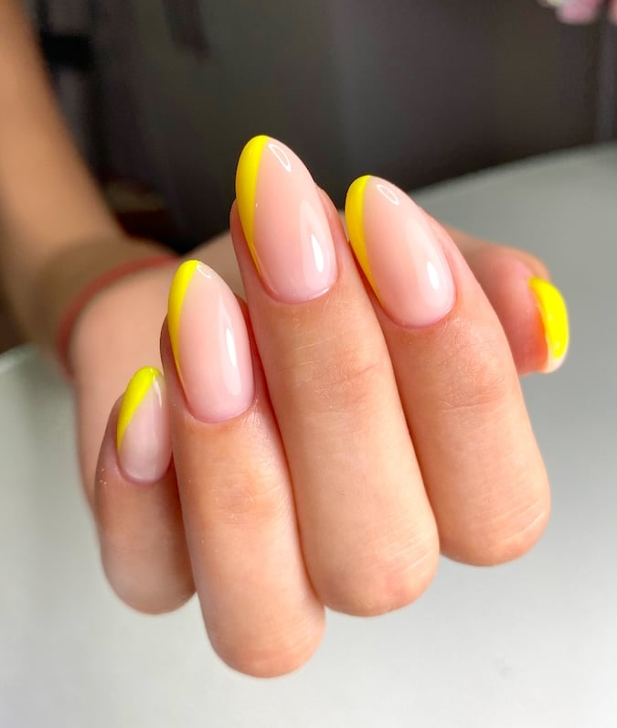 Bright yellow angled French tip almond nails.