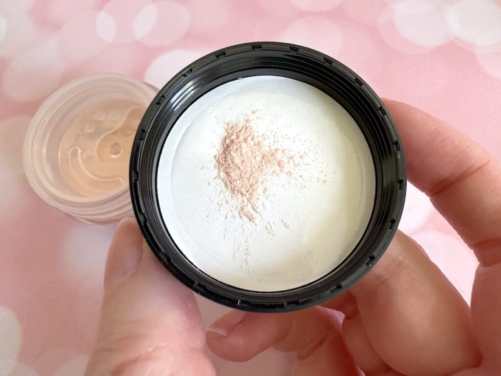 bareMinerals Original Mineral Veil Loose Setting Powder in the shade Original Translucent. Open jar with powder sample on inside of cap, handheld.