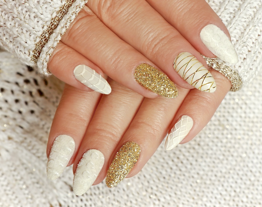 Beige gold knit winter nails surrounded by cream knit sweater.