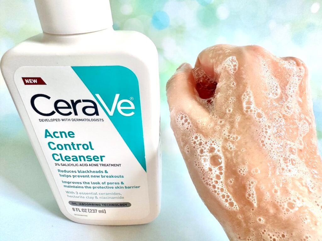 CeraVe Acne Control Cleanser bottle next to cleansing foam sample on back of hand.