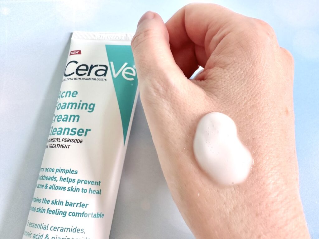 CeraVe Acne Foaming Cream Cleanser, flatlay of tube next to sample on hand.