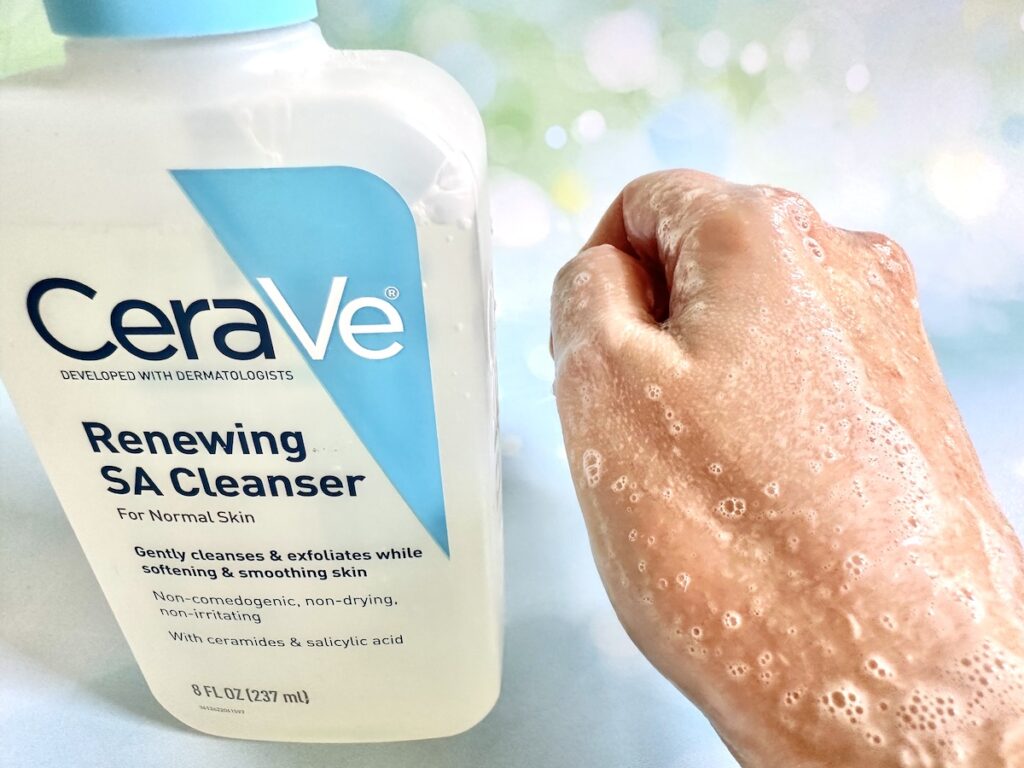 CeraVe Renewing SA Cleanser bottle next to foam sample on back of hand.