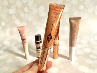 Charlotte Tilbury Highlighter Wand, handheld, in front of four drugstore dupes.