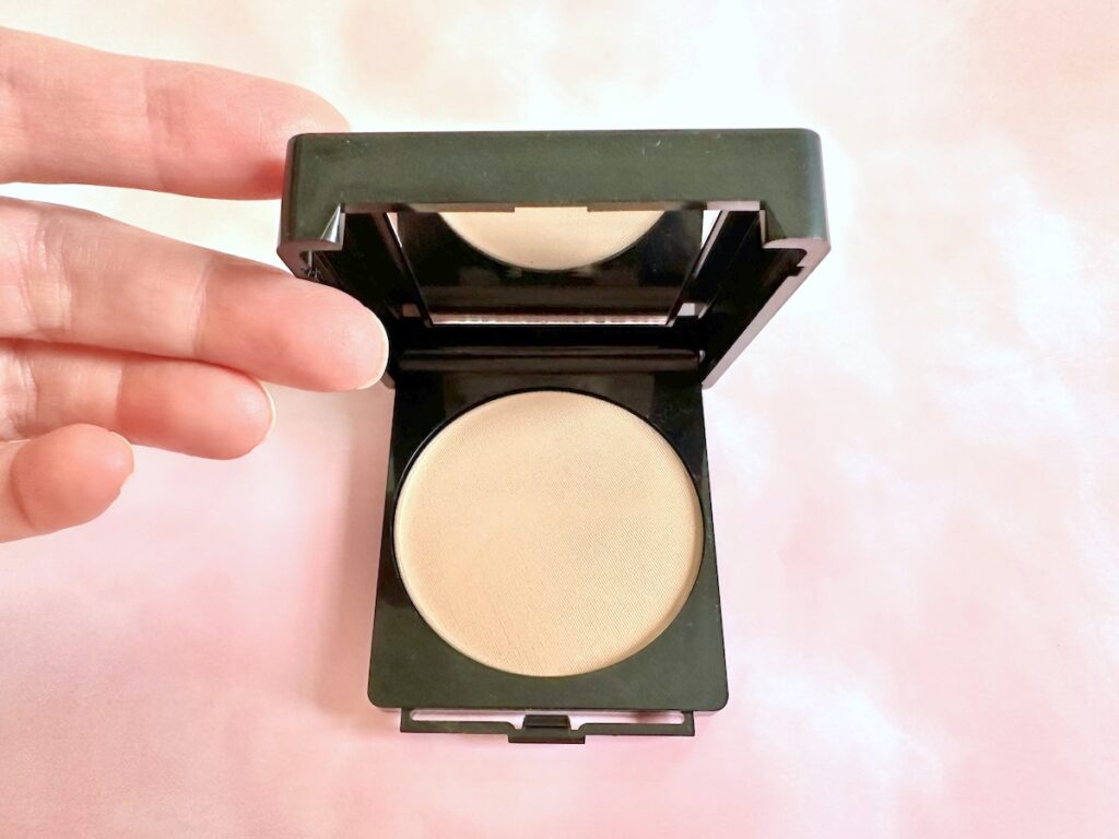 CoverGirl Clean Powder Foundation in the shade Buff Beige, compact being held open by hand, flatlay.