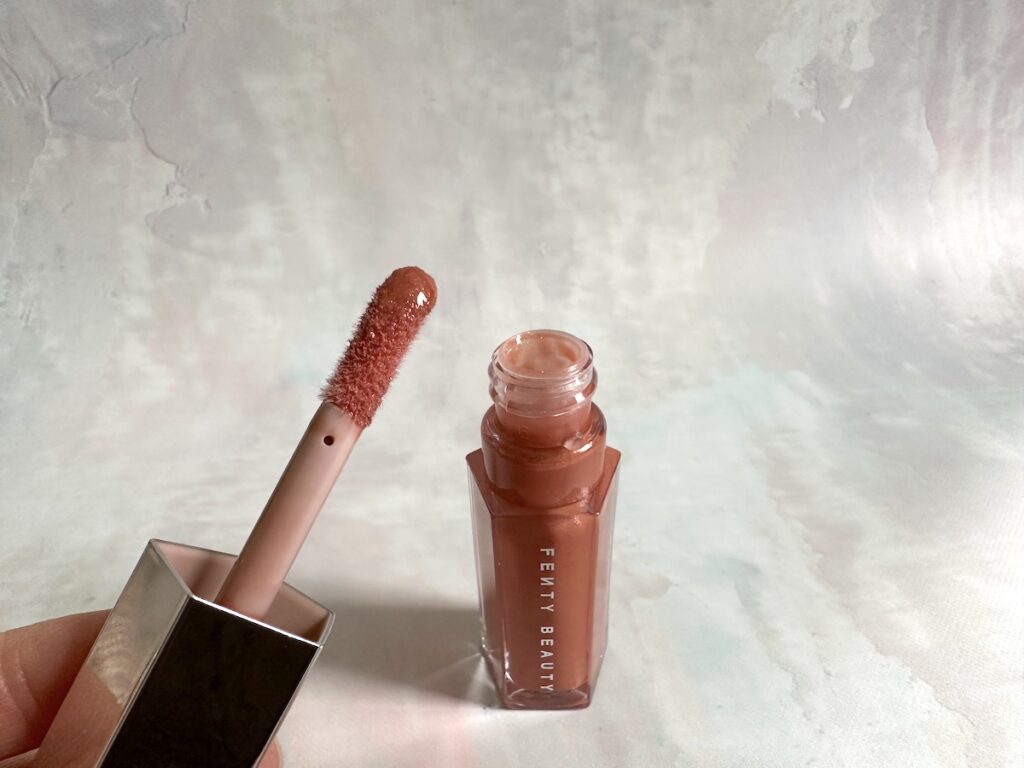 Fenty Gloss Bomb Universal Lip Luminizer in the shade Fenty Glow, open with doe-foot applicator.