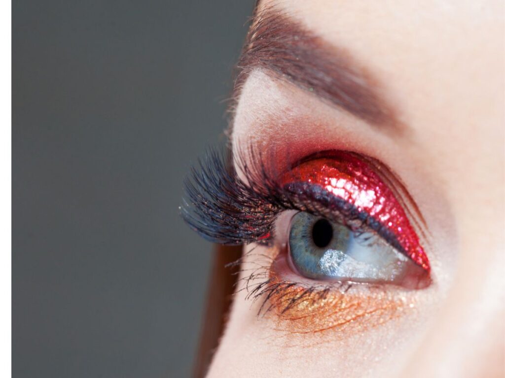 Metallic red and gold glitter eyeshadow on eye with long lashes.