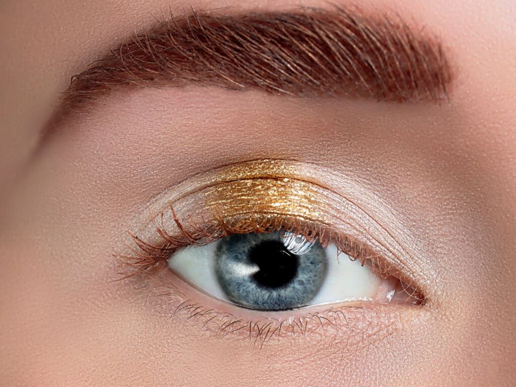 Gold glittery eyeshadow in the center of the eyelid of a blue eye.