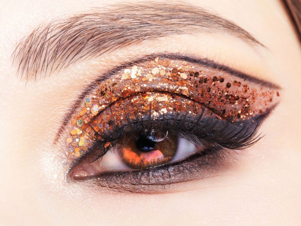 Chunky gold flakes add dimension and texture over a smoky brown base and eyeliner arched on eyelid.