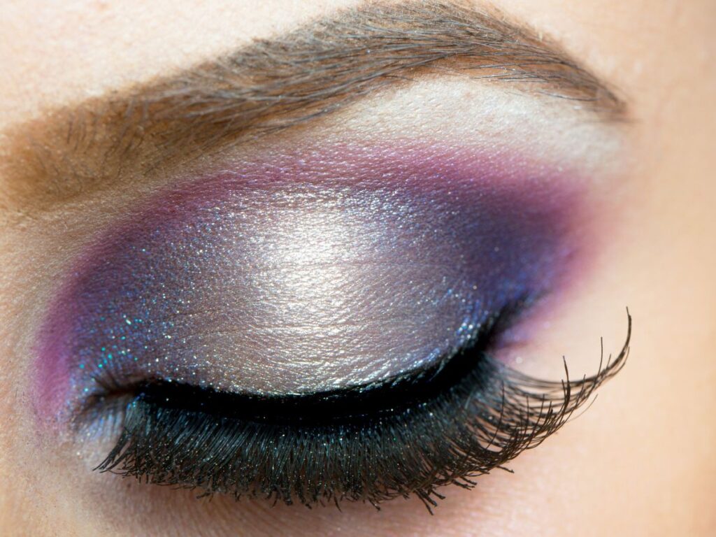 Purple, blue and silver glitter eyeshadow on closed eye with false lashes.