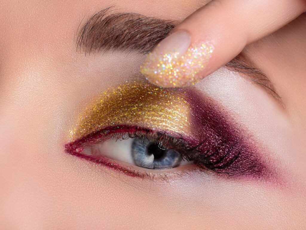 Burgundy and glod glitter eyeshadow with finger applying more gold eyeshadow.