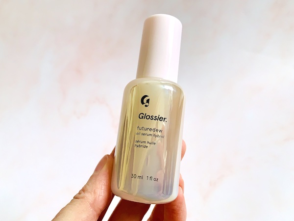 Glossier Futuredew Oil Serum Hybrid hand-held on pink background