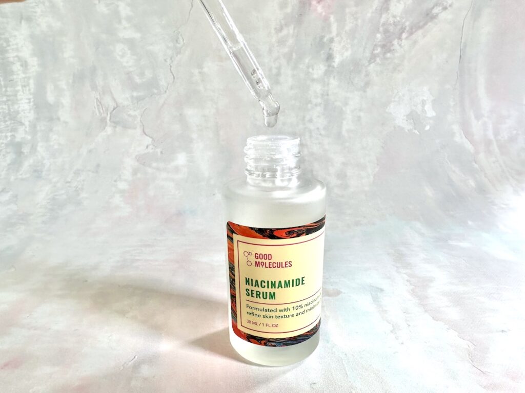 Good Molecules Niacinamide Serum, handheld., open bottle with dropper applicator.