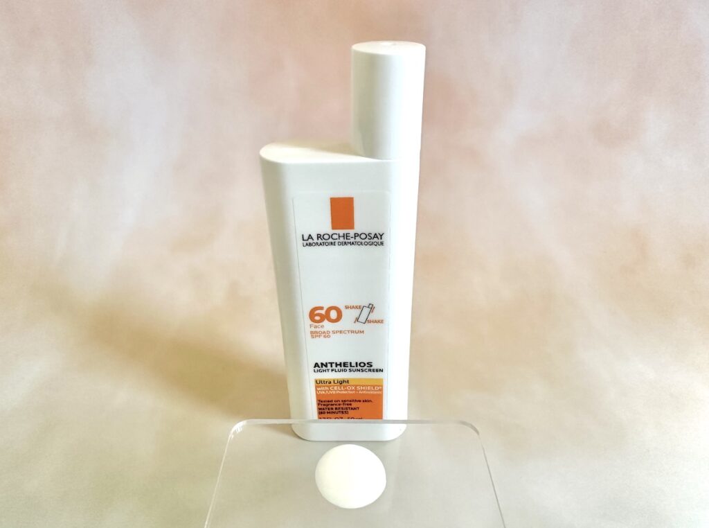 La Roche-Posay Anthelios Light Fluid Sunscreen SPF 60, bottle behind sunscreen sample on clear plastic spatula.