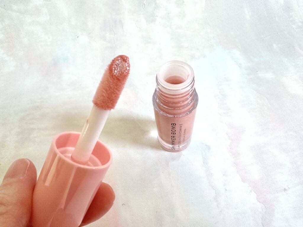 Makeup Revolution Shimmer Bomb Lip Gloss in the shade Glimmer, open tube with extra large doe-foot applicator, handheld.