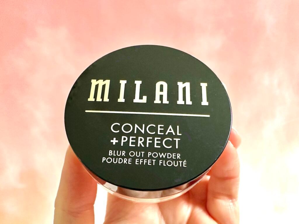 Milani Conceal + Perfect Blur Out Powder in the shade Translucent, handheld.