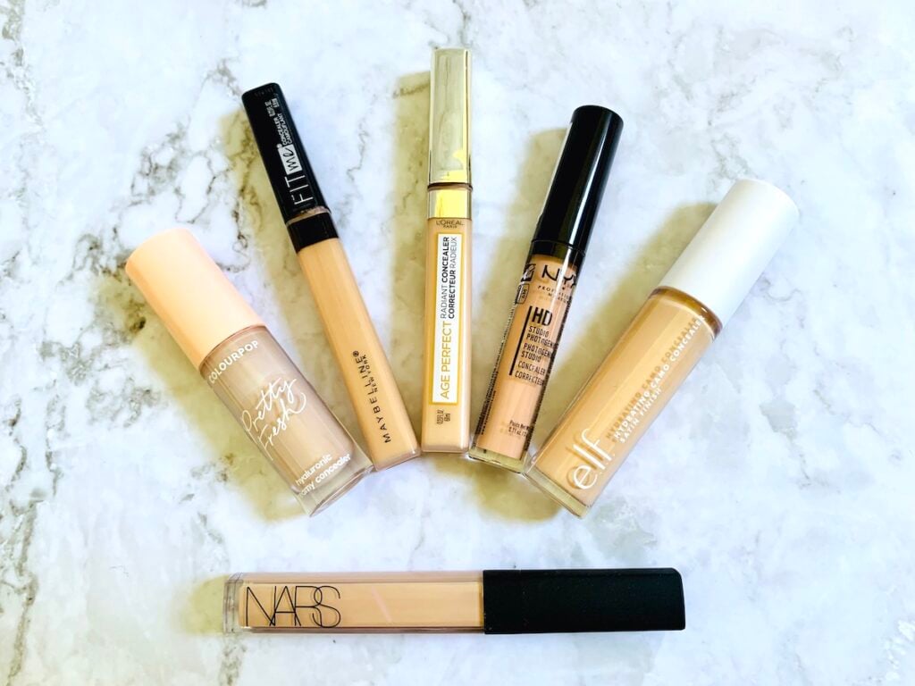 Flatlay of NARS Concealer and drugstore dupes from elf, Maybelline, L'Oreal, NYX and ColourPop: concealer dupes arranged in an arc above NARS