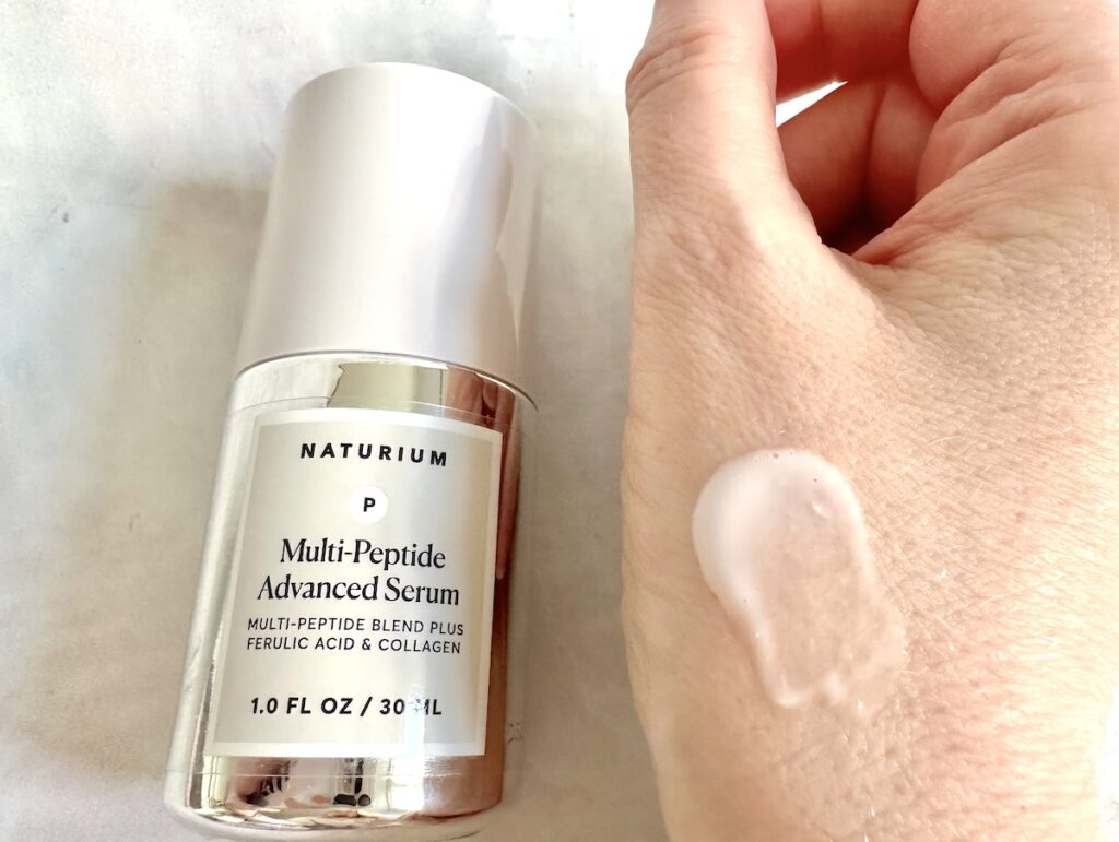 Naturium Multi-Peptide Advanced Serum, bottle flatlay next to sample on hand.