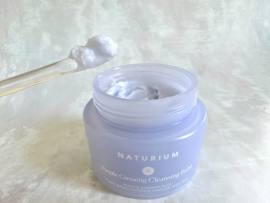 Naturium Purple Ginseng Cleansing Balm, open jar with sample on clear plastic spatula.