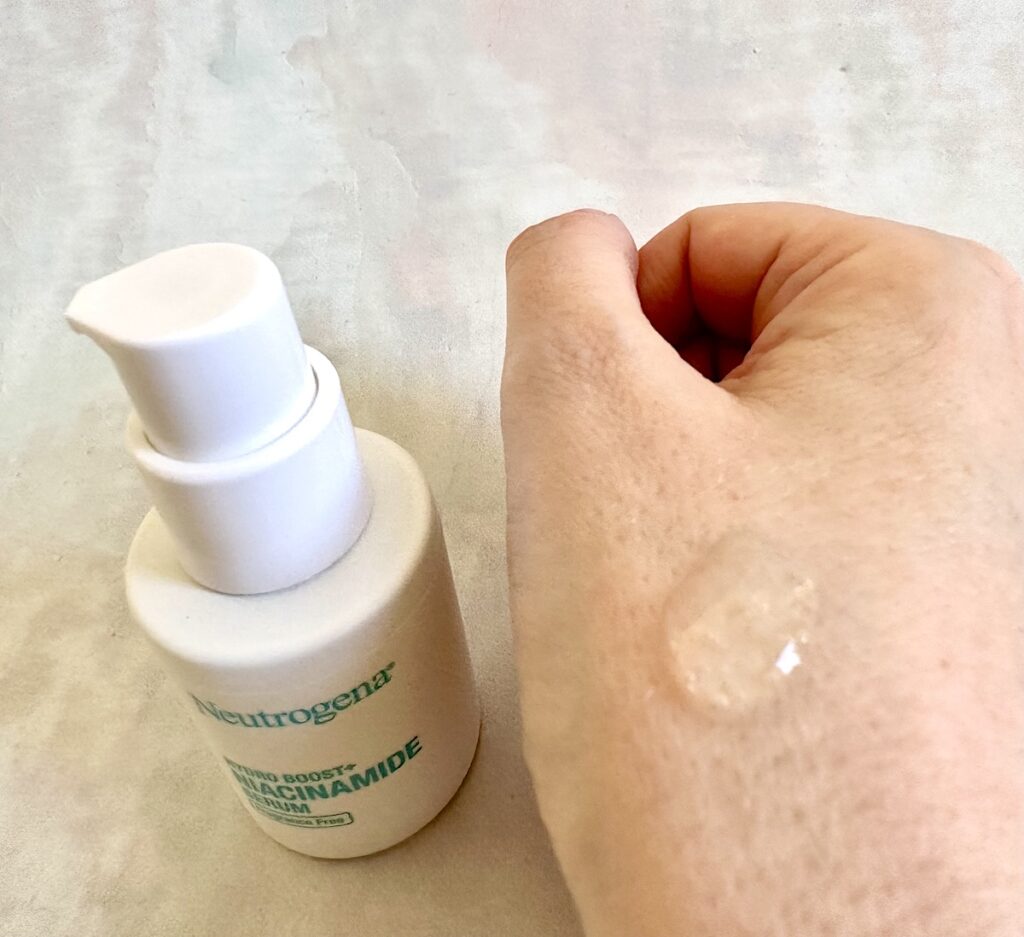 Neutrogena Hydro Boost+ Niacinamide Serum bottle next to clear serum sampled on hand.