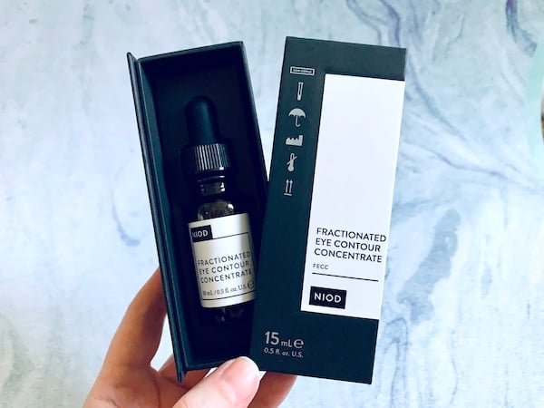 NIOD Fractionated Eye Contour Concentrate held by hand in box on blue background