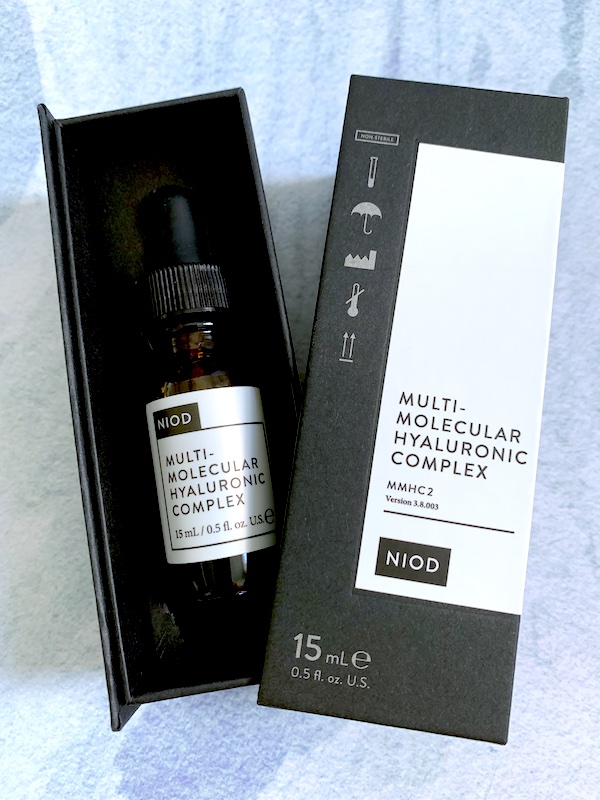 Flatlay of NIOD Multi-Molecular Hyaluronic Complex in opened two piece box on blue background