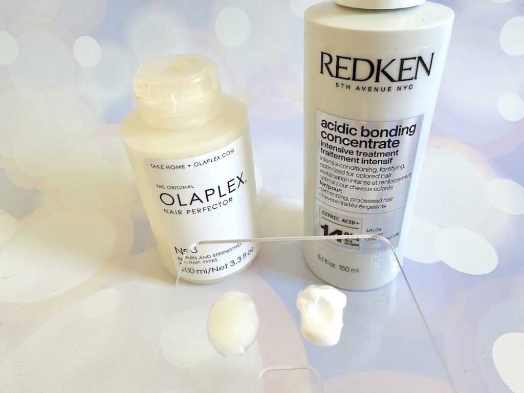 Olaplex No.3 Hair Perfector and Redken Acidic Bonding Concentrate Intensive Treatment bottles behind samples on clear plastic spatula.