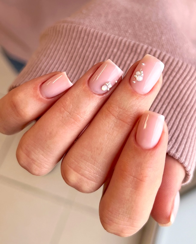 Pink nails, two of which are decorated with moonstones and silver beads.