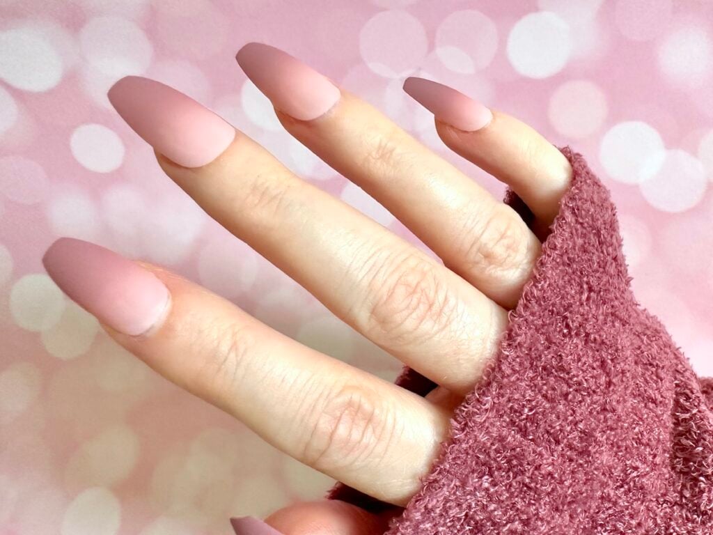 Press on pink ballerina fall ombre nail on right hand with dark mauve sweater sleeve.