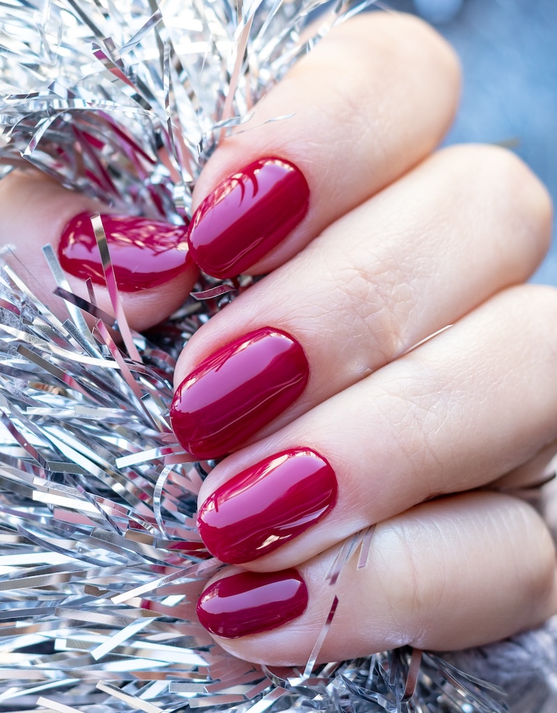 Red glossy winter nails holding silver tinsel.