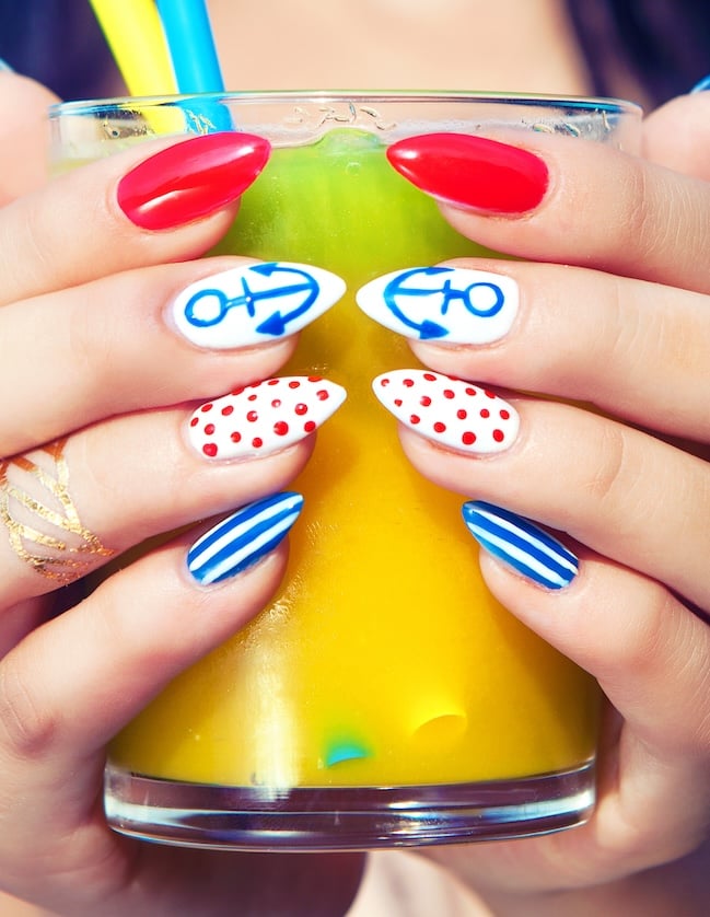 Red, white and blue sailor nails on women holding a glass of orange juice with straw.