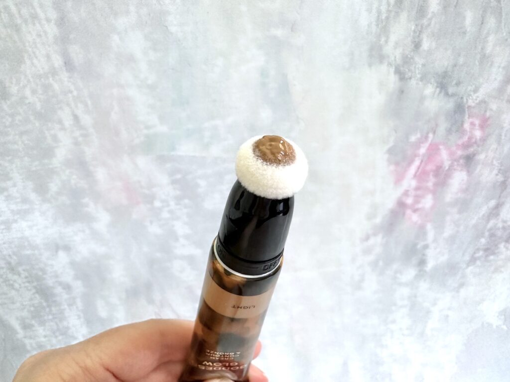 Revolution Pro Goddess Glow Cream Contour & Bronze in the shade Light, open tube with cushion applicator handheld.