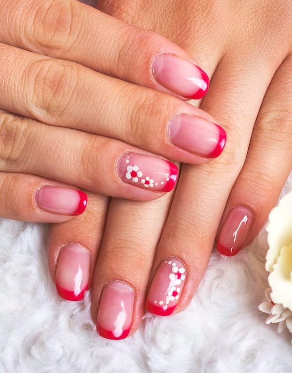 Pink/red French tip nails with floral nail art.