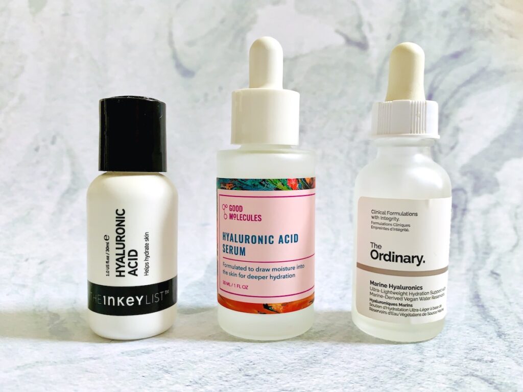 The Inkey List Hyaluronic Acid Serum, Good Molecules Hyaluronic Acid Serum, and The Ordinary Marine Hyaluronics Serum on a pale blue background.