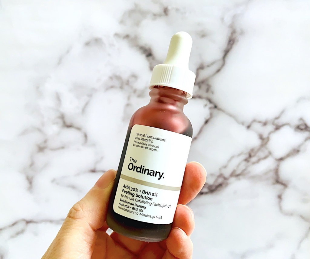 The Ordinary AHA 30% + BHA 2% Peeling Solution held by a hand in front of a marble background