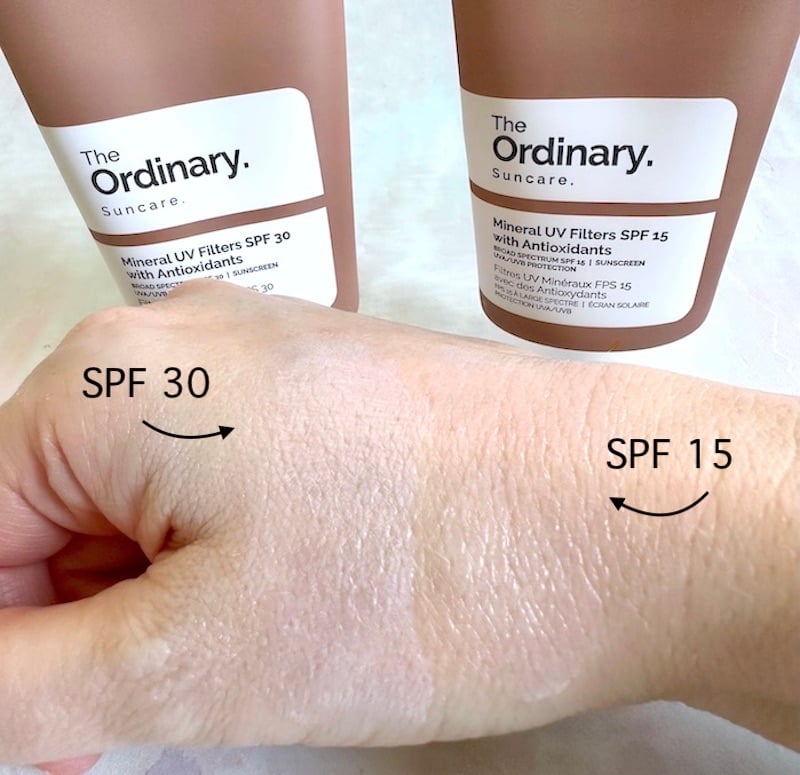 The Ordinary Mineral UV Filters SPF 30 with Antioxidants and The Ordinary Mineral UV Filters SPF 15 with Antioxidants tubes next to samples rubbed into hand showing white cast, labeled SPF 30 and SPF 15.