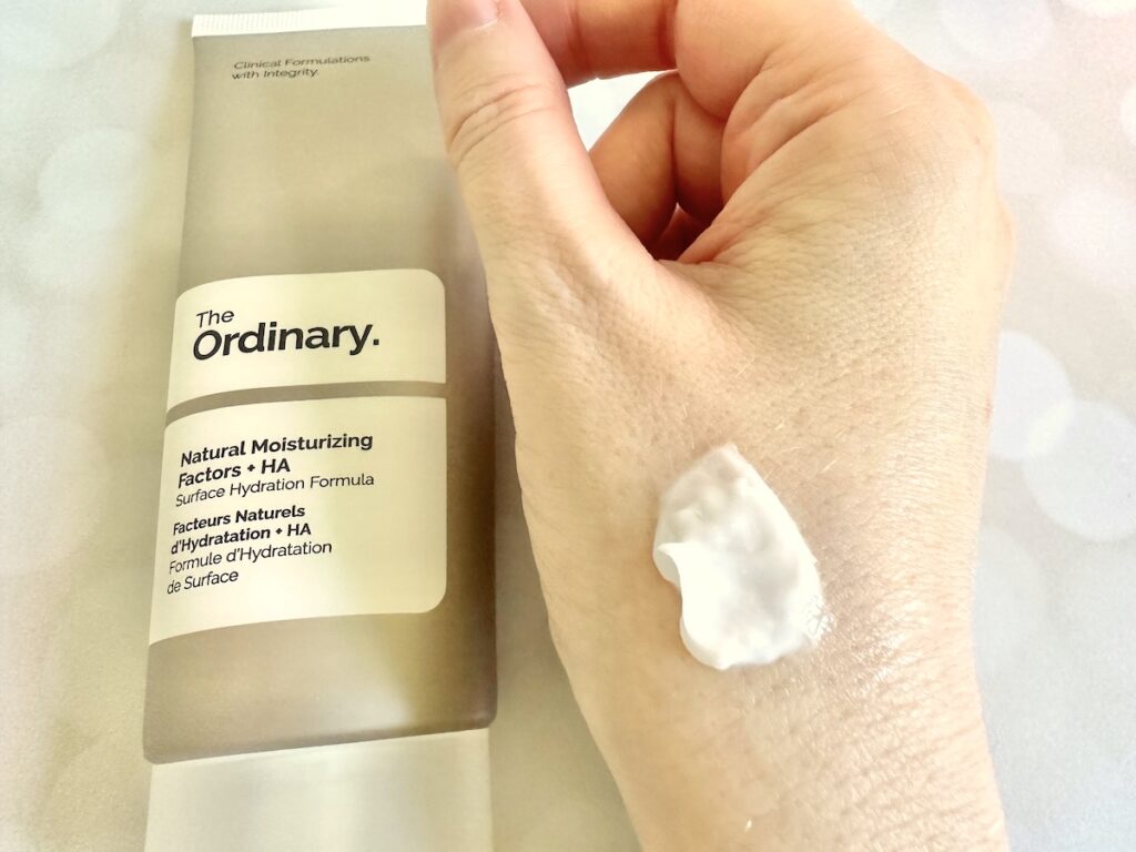 The Ordinary Natural Moisturizing Factors + HA, flatlay of tube next to sample on hand.