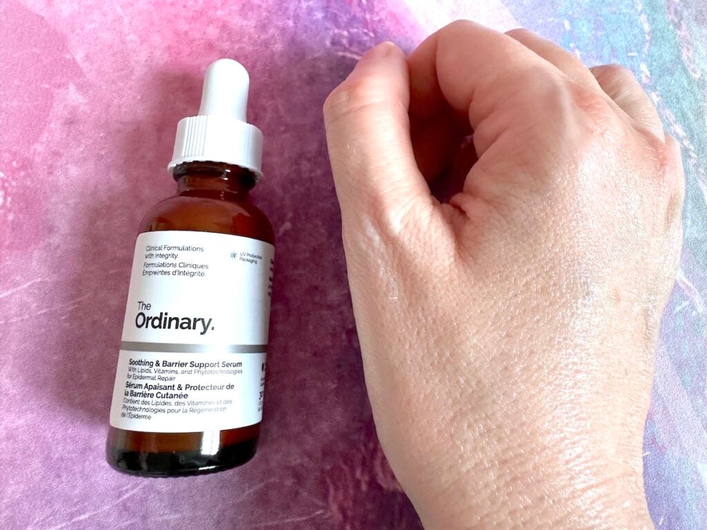 The Ordinary Soothing & Barrier Support Serum, flatlay of bottle next to a few drops of pink serum on hand, absorbed.