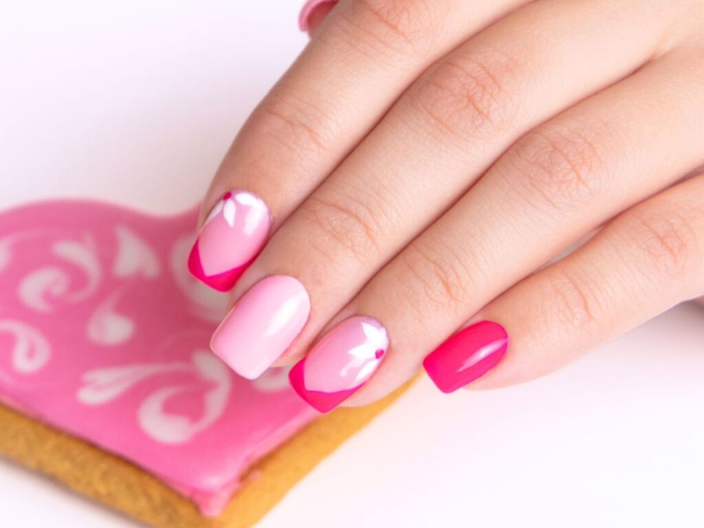 Pink, white and dark pink Valentines nails with nail art in front of a pink heart cookie.