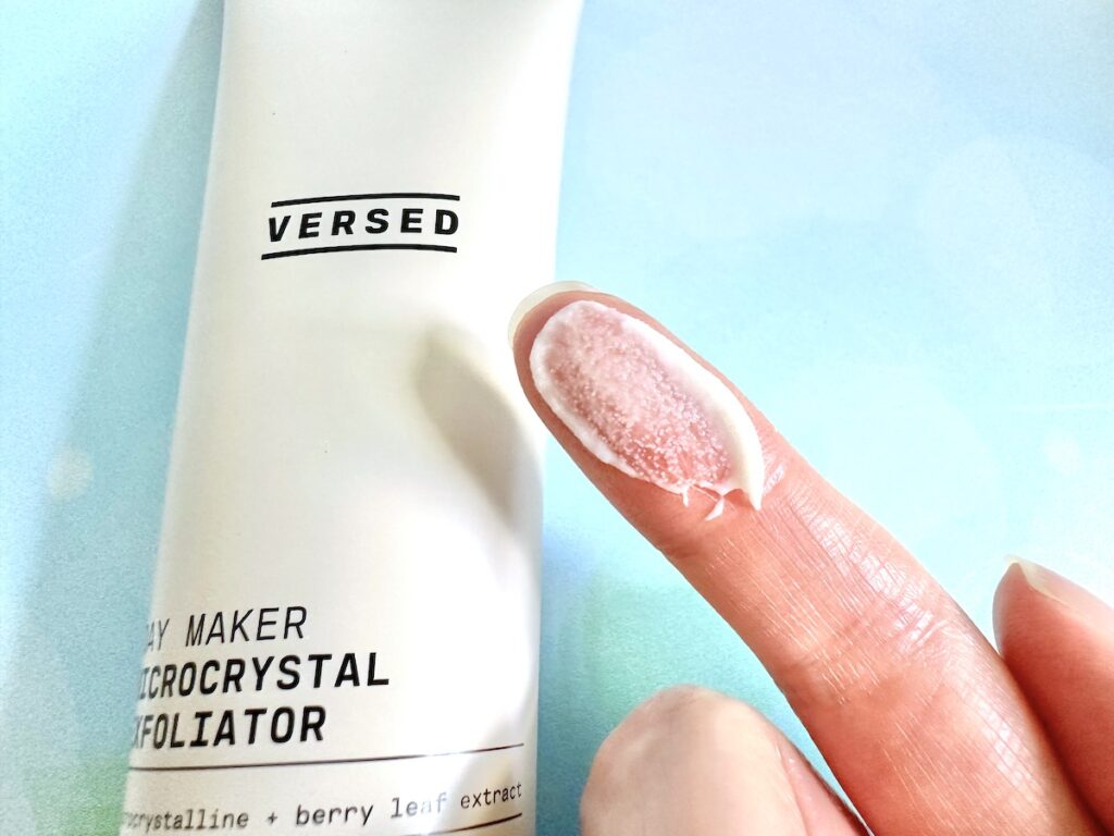 Versed Day Maker Microcrystal Exfoliator, flatlay of tube next to sample on finger.