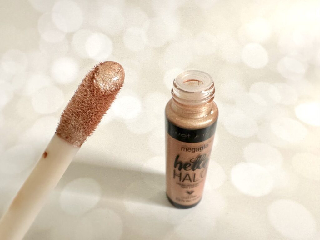 Wet n Wild MegaGlo Halo Liquid Highlighter in the shade Guilded Glow, open bottle with applicator wand, handheld.