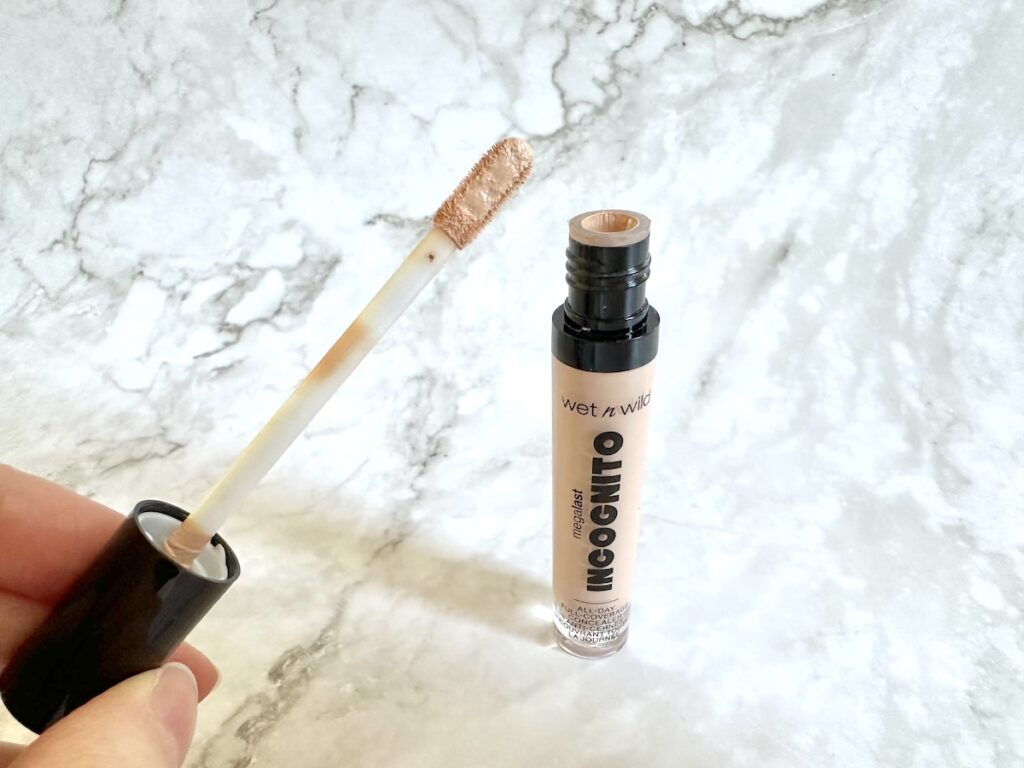 Wet n Wild Megalast Incognito All Day Full Coverage Concealer, open tube with flat applicator wand, handheld.