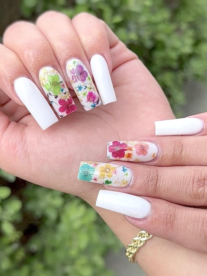 White nails with colorful flowers. Outside near greenery.