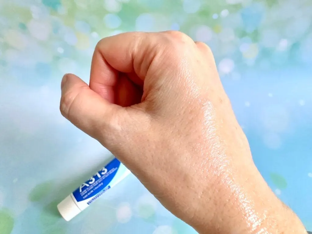 A313 Cosmetic Cream With Retinyl Palmitate, flatlay of tube next to sample on hand absorbed.