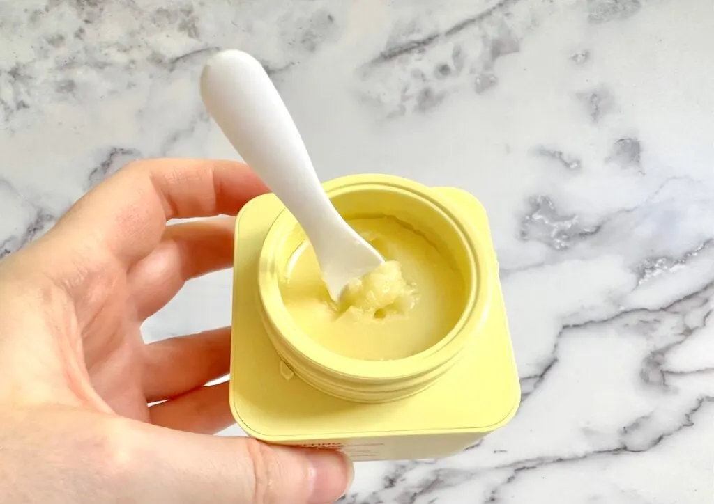 Byoma Melting Balm Cleanser Cleansing Balm, open jar with white cosmetic spatula, handheld.