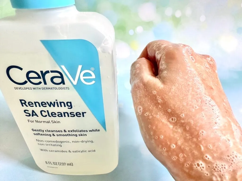 CeraVe Renewing SA Cleanser bottle next to foam sample on back of hand.