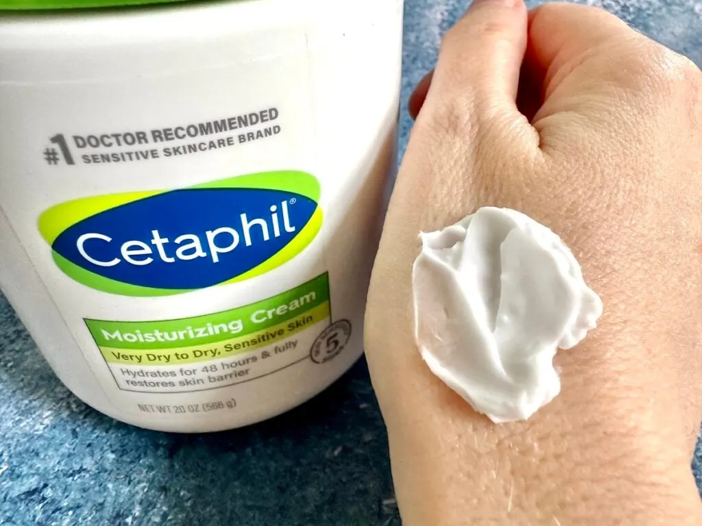 Cetaphil Moisturizing Cream tub next to cream sampled on back of hand.