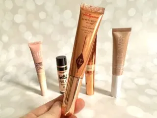 Charlotte Tilbury Highlighter Wand, handheld, in front of four drugstore dupes.